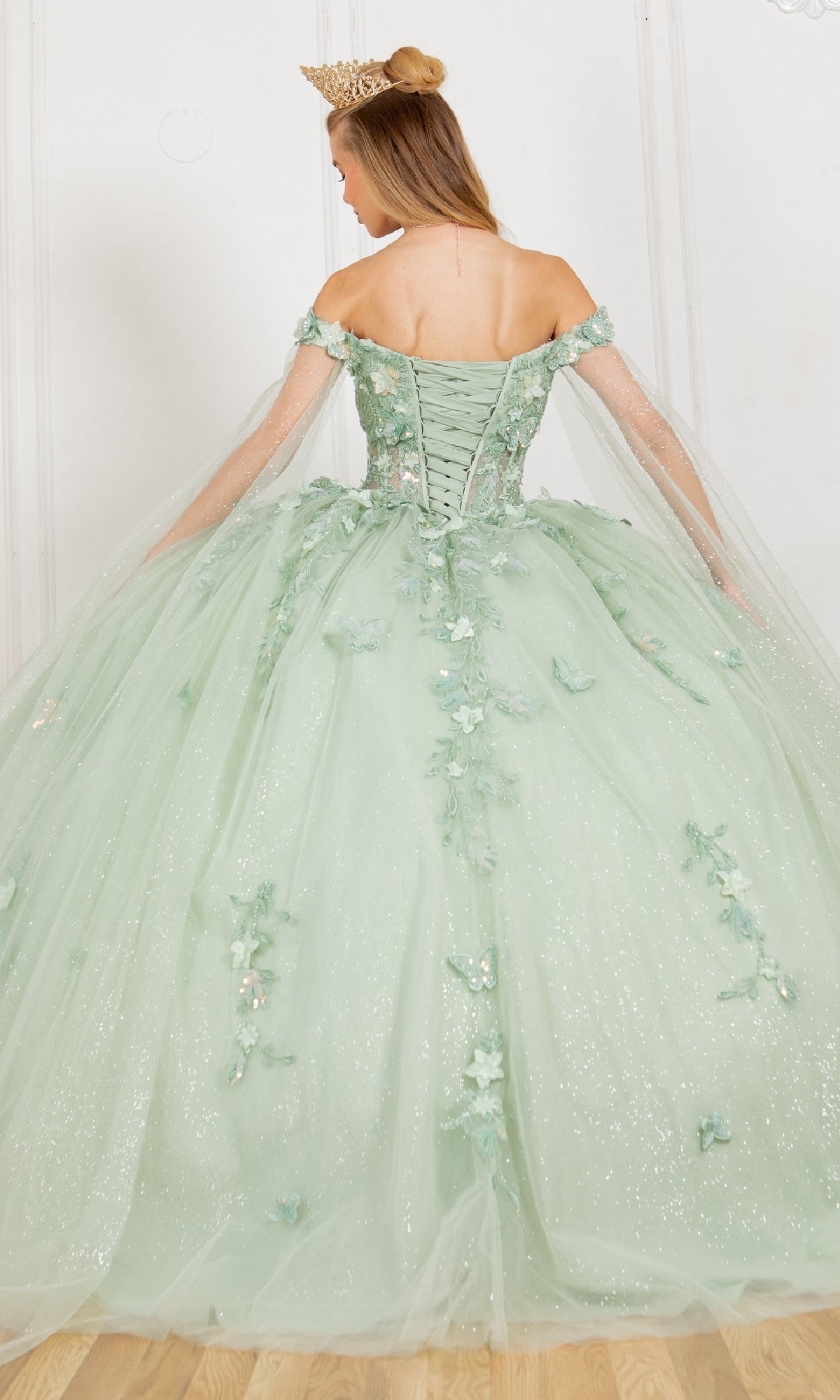Woman shown from the back wearing Cinderella Couture 8075J, a sparkling pale green off-the-shoulder quinceanera dress with floral 3D appliques and a crown.